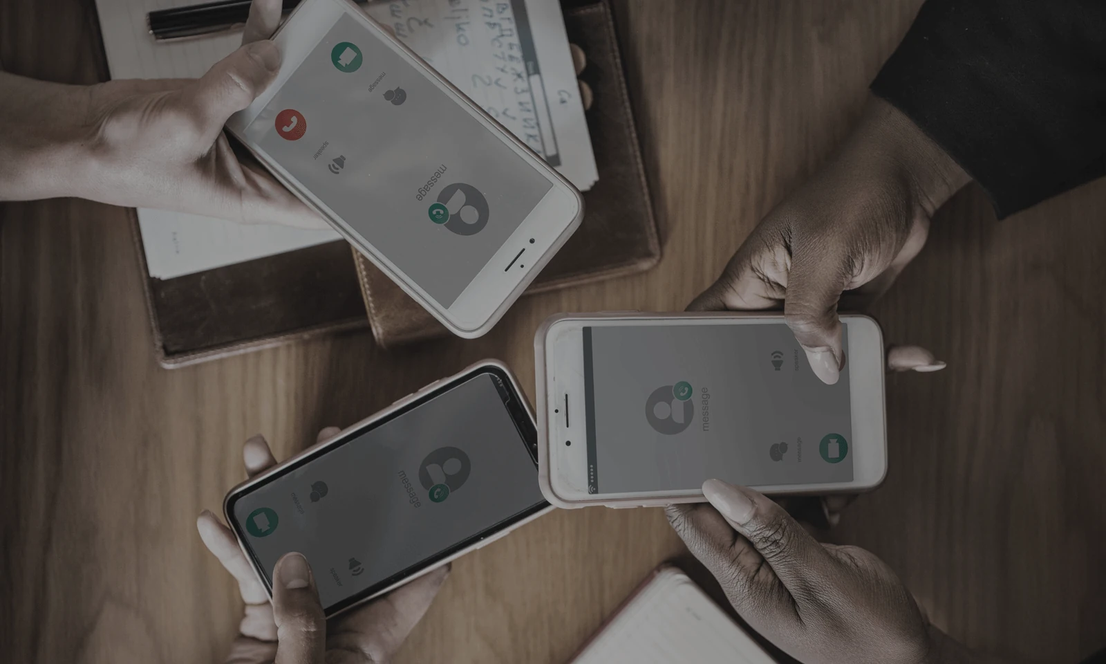 Three people holding smartphones with an incoming call screen over a wooden table