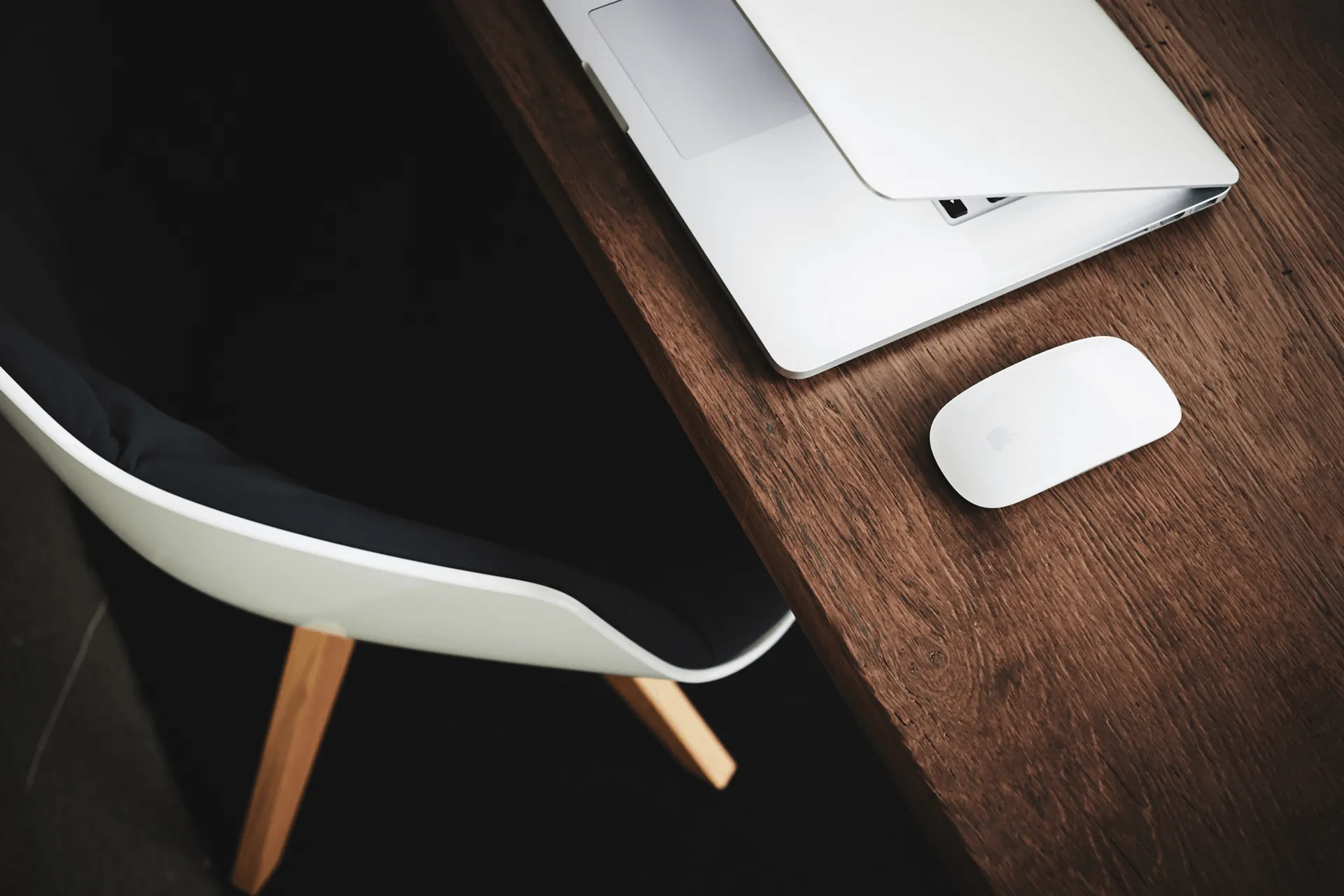 Laptop and wireless mouse on a wooden desk beside an office chair