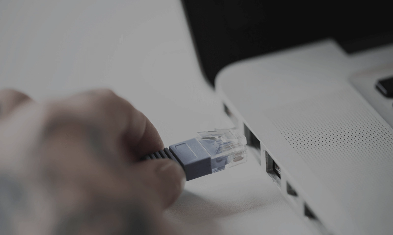 Close-up of a hand plugging an Ethernet cable into a laptop
