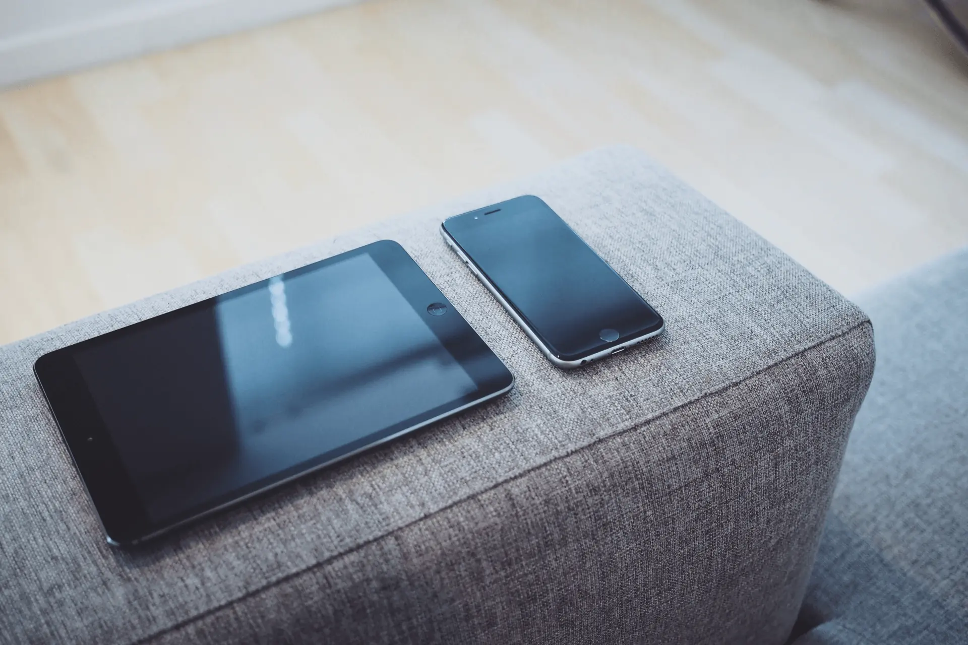 Tablet and smartphone resting on a grey fabric sofa armrest