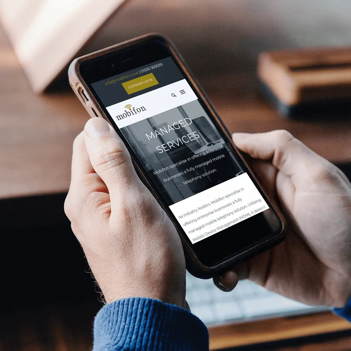 Person holding a smartphone displaying the Mobifon Managed Services webpage.